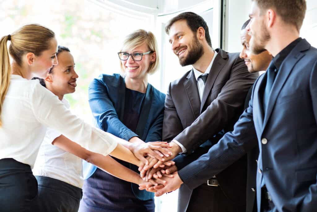Eine Gruppe von Arbeitskollegen hat ihre Hände in der Mitte gemeinschaftlich aufeinandergelegt.