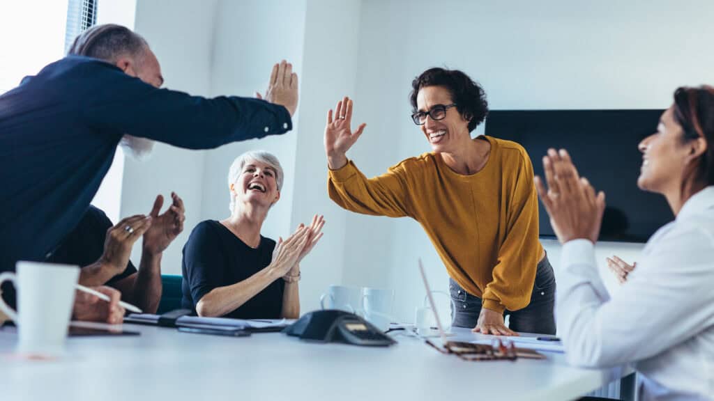 Zwei Mitarbeitende geben sich ein High-Five, während ihre Kollegen und Kolleginnen um sie herum applaudieren.