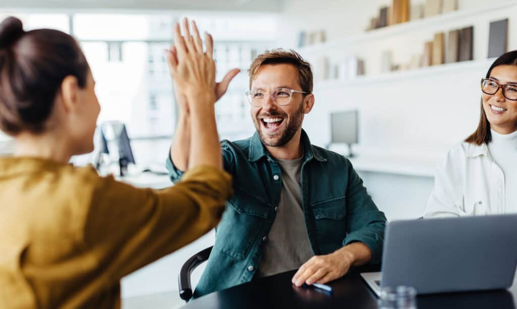 Ein Mitarbeiter und eine Mitarbeiterin geben sich im Büro lachend ein High-Five.